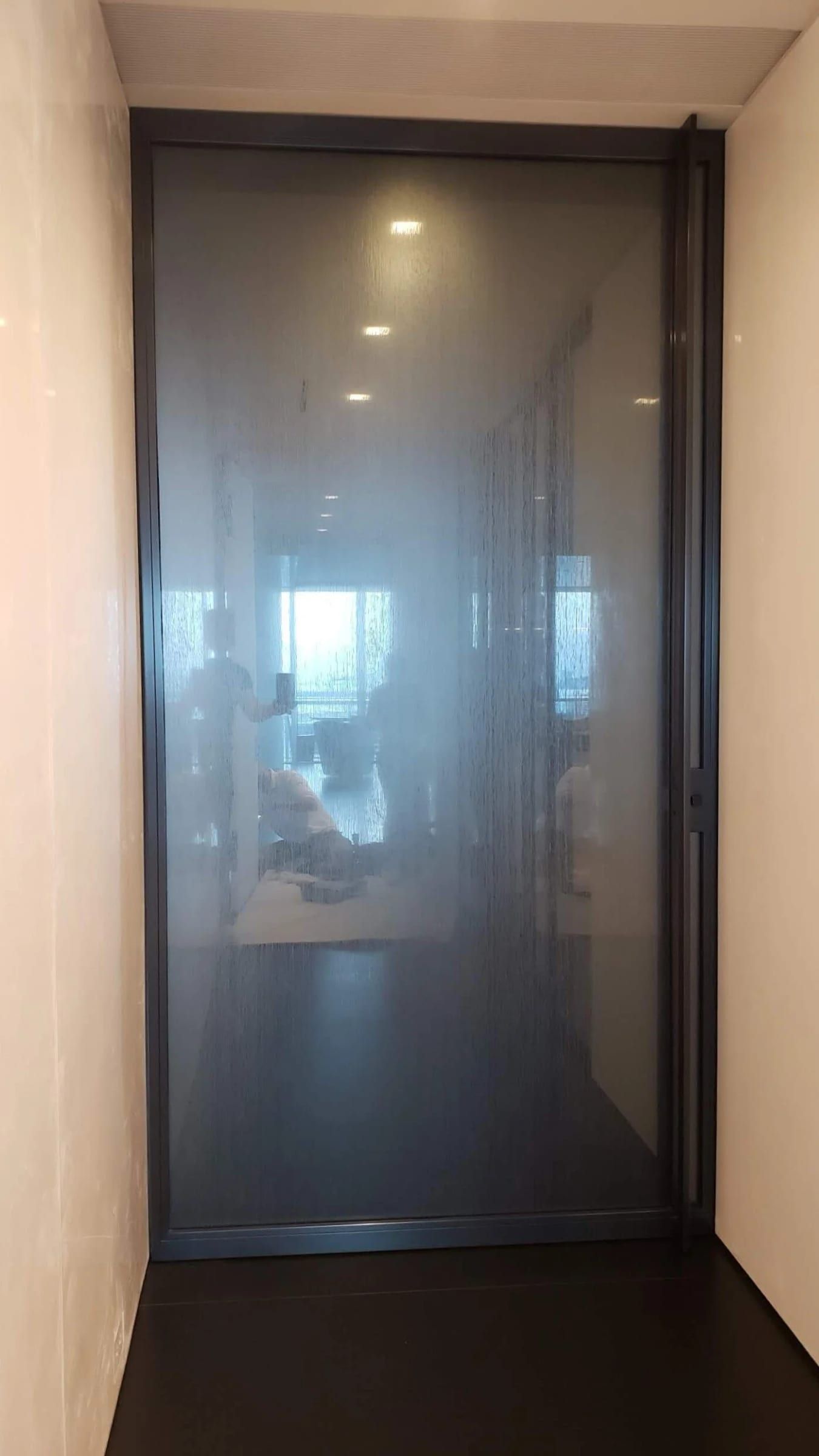 Tall blackened stainless door with frosted glass at the end of a corridor