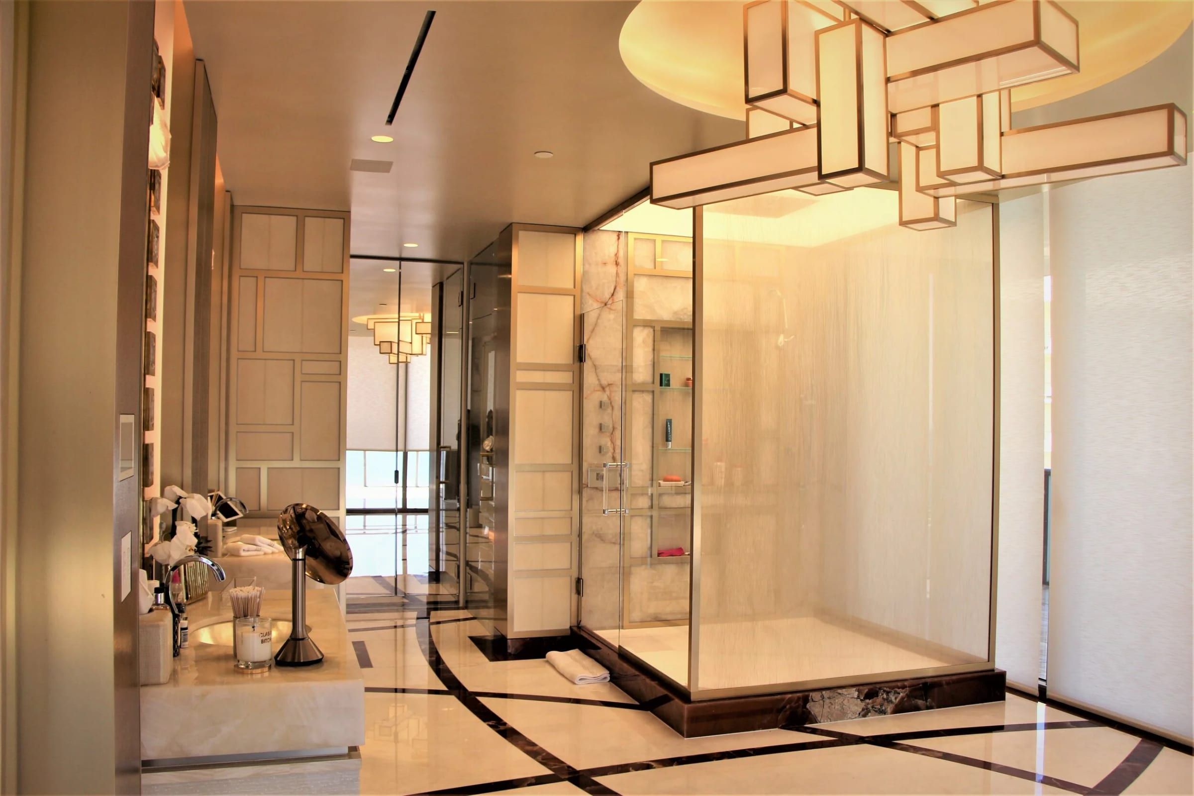 Bathroom with a brass-framed glass enclosure under a sculptural light